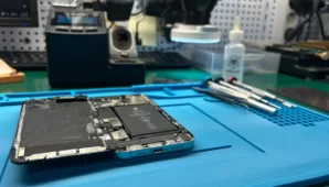 iPhone abierto sobre manta ESD durante reparación — flex de pantalla y entorno de taller