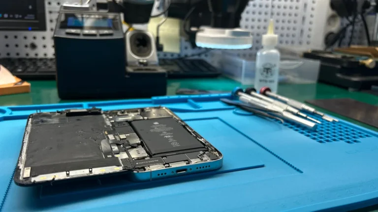 iPhone abierto sobre manta ESD durante reparación — flex de pantalla y entorno de taller
