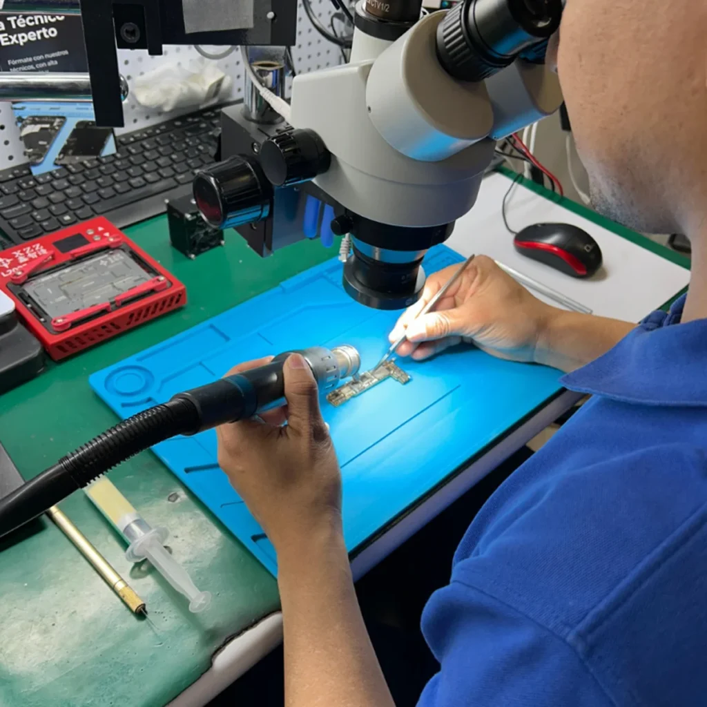 Técnico desoldando IC táctil de pantalla iPhone con estación de calor bajo microscopio