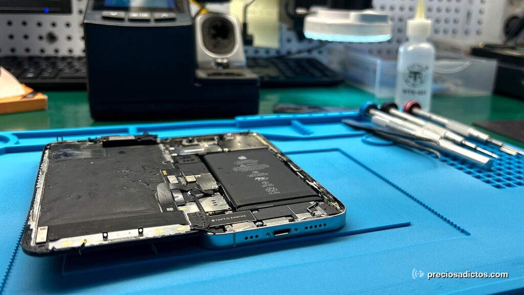 Un iPhone abierto sobre el banco de reparación de Preciosadictos, con la batería a la vista